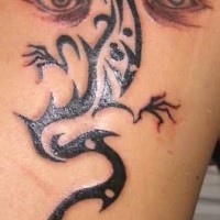 El tatuaje de una lagartija tribal en color negro y ojos humanos en la espalda