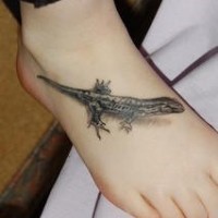 El tatuaje de una lagartija pequeña de color negro en el pie