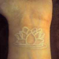 el tatuaje sencillo lineado de una flor de loto hecho con tinta blanca en la muñeca