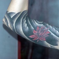 el tatuaje de una flor de loto roja en un fondo negro hecho en el brazo