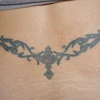 Lower back tattoo, cross with stone in curled pattern