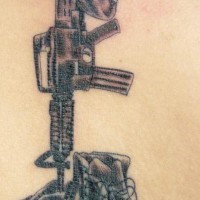 el tatuaje memorial de un m16 con una botas y un casco hecho en la espalda en color negro