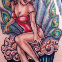el tatuaje estilo pin up con una chica sobre un cupcake y las plumas del pavo real