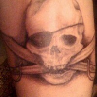 el tatuaje de tinta gris con una calavera pirata con cuchillos cruzados en su boca