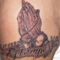 El tatuaje Conmemorativo de las manos orantes con las fechas de la vida hecho en color negro