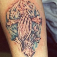 el tatuaje colorado de las manos orantes sobre una cruz