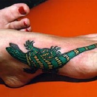 Pequeño tatauje de lagartija en verde y amarillo en el pie