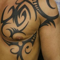 Tatuaggio grande non colorato sul deltoide e sul petto il disegno in stile tribale