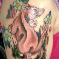 Tatuaje del ratoncito entre las flores y hierba en el hombro