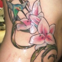 Le tatouage de flanc d'un joli colibri volant près d'une fleur