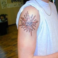 Calavera en el símbolo del sol tatuaje en el brazo