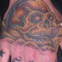 Un crâne sablé riant avec le tatouage de prénom sur la main
