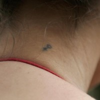 Tatuaje con pequeño simbolo femenino en la nuca