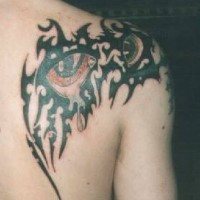 Tatuaje tribal tinta negra en el hombro y omoplato con los ojos en color