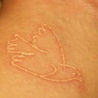 White ink tattoo with bird on wrist