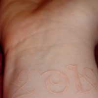 White ink tattoo with year on wrist