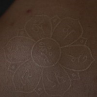 White ink tattoo with yoga flower