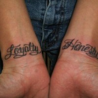 Kalligraphisches Tattoo mit Worten Loyalität und Ehrlichkeit an beiden Handgelenken
