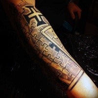 Tiny black and white forearm tattoo of puzzle picture stylized with cross