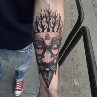 Tribal style black in mask tattoo on forearm stylized with triangle shaped symbols and trees
