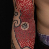 Tatuaje en el brazo, ornamento de colores negro y rojo con compás pequeño