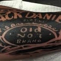 Typical blackwork style arm tattoo of Jack Daniels bottle lettering