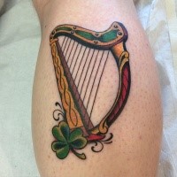 Typical illustrative style colored leg tattoo of harp with clover leaf
