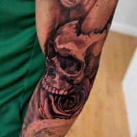 Usual black ink broken human skull tattoo on half sleeve with rose
