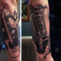 Üblich kombiniertes großes schwarzes und weißes detailliertes Mikrofon mit Gitarre Tattoo am Arm