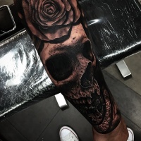 Very detailed black human skull tattoo on forearm with rose