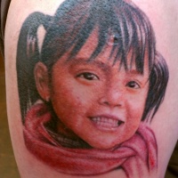 Very realistic looking cute smiling colored girl portrait tattoo on thigh