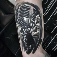 Tatuaje de micrófono con mano en el brazo, colores negro blanco