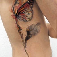Tatuaggio colorato sul fianco la farfalla incantevole sul fiore