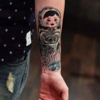 Watercolor style colored forearm tattoo of Matryoska doll with lettering