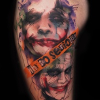 Watercolor style colored thigh tattoo of Joker face with lettering