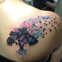 Tatuaje en el omóplato en acuarela de arboles con pájaros.