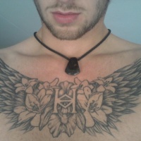 Wings with anagram and flowers tattoo on chest