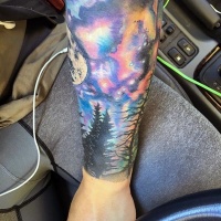 Wonderful and colorful night sky in forest tattoo on arm