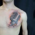 Tatuaje  de micrófono retro pequeño con notas en el pecho