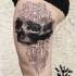 Abstract style black ink thigh tattoo of human skull with ornaments