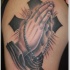 Tatuaje en el brazo,
cruz grueso negro y manos que oran