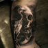 Black and gray style small biceps tattoo of human skull with little bird skeleton
