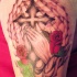 Tatuaje en el brazo, cruz de hierro con manos que oran y rosas, estilo cristiano