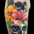 Tatuaje en el brazo, dos cráneos negros, flores amarillo y rosa