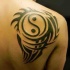 Cool sharp dark black ink Yin Yang special stylized symbol tattoo on man's shoulder blade with tribal elements