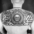 Dark black ink upper back tattoo of human skull with various symbols