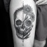 Engraving style black ink thigh tattoo of human skull with flowers