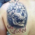 Funny looking black ink shoulder tattoo of puzzle picture stylized with human skull and lettering