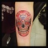Funny smiling multicolored skull in Mexican style forearm tattoo