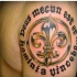 dorato fleur de lis e scrittura nera tatuaggio sulla spalla